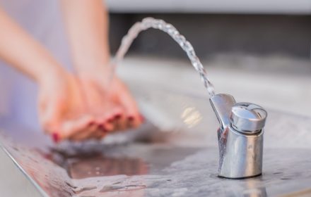 Closeup on woman hand catching water. Splashing drops on sunny summer outdoors background. Environment and health concept. Flowing Fountain Cool Drink