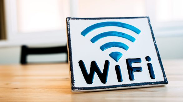 White square badge with sign of wireless connection for gadgets on wooden surface